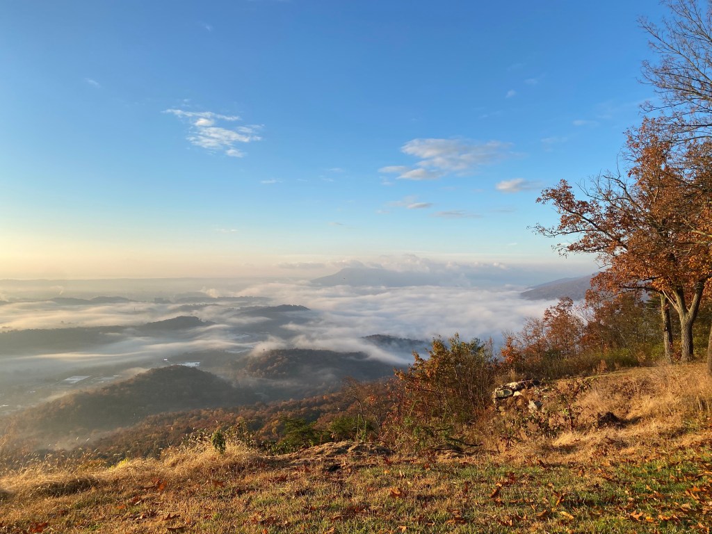 Image taken from top of mountain showing fog settling over mountains in background.