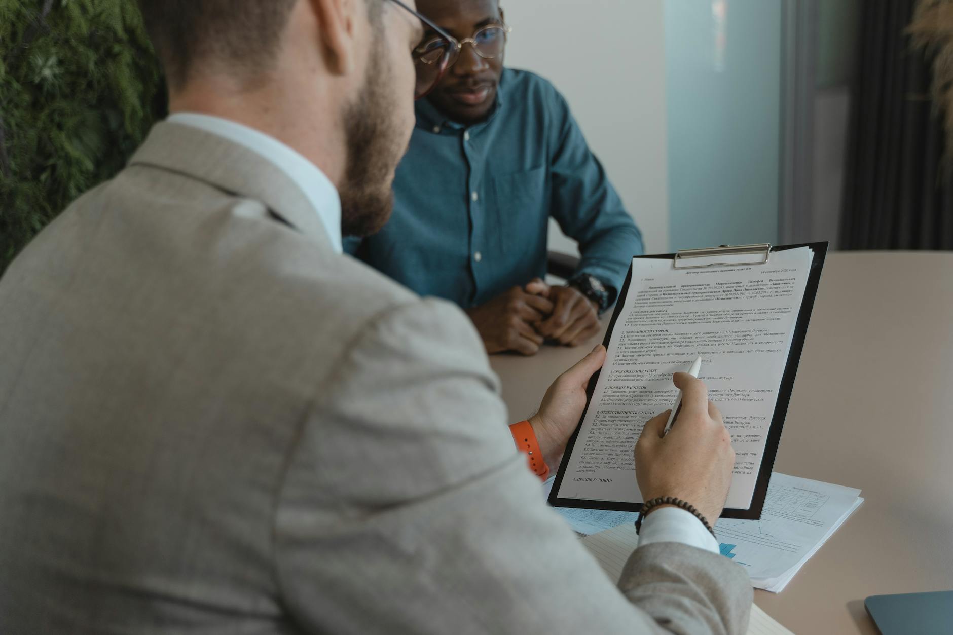 Two men sitting, with one looking at the other's resumé.